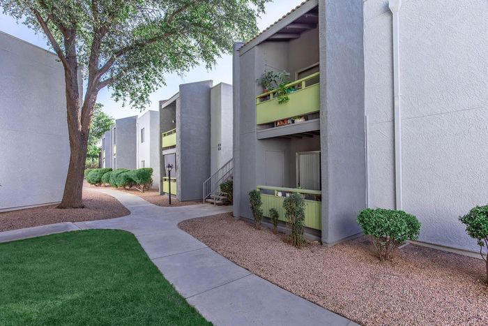 Charming apartment exterior with green accents, set amidst lush landscaping and sunlit walkways.