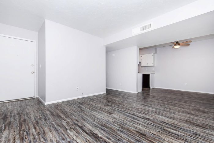 Bright and spacious living area with modern wood flooring and an open kitchen layout, featuring ceiling fan and ample natural light.