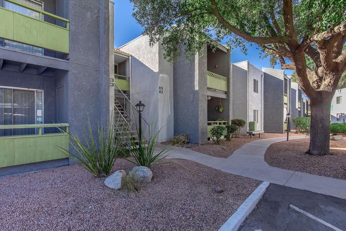 Charming apartment exterior with modern design, vibrant green accents, and lush landscaping under a clear blue sky.