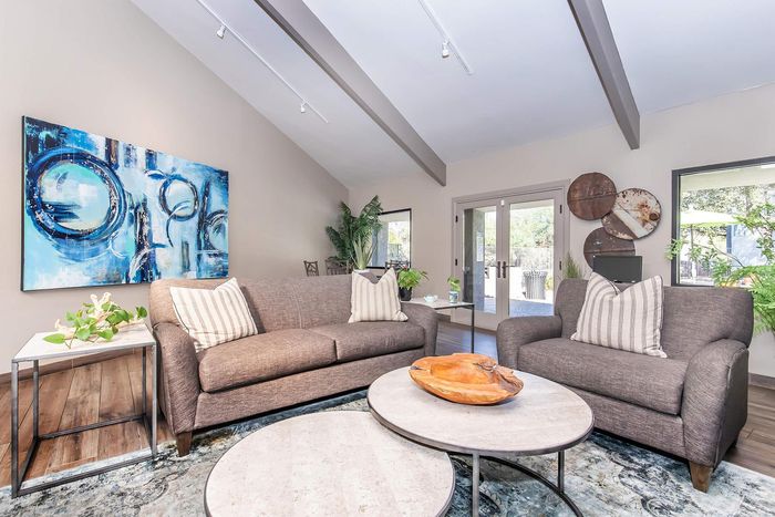 Bright and inviting living room with modern art, cozy sofas, and large glass doors opening to a lush garden view.