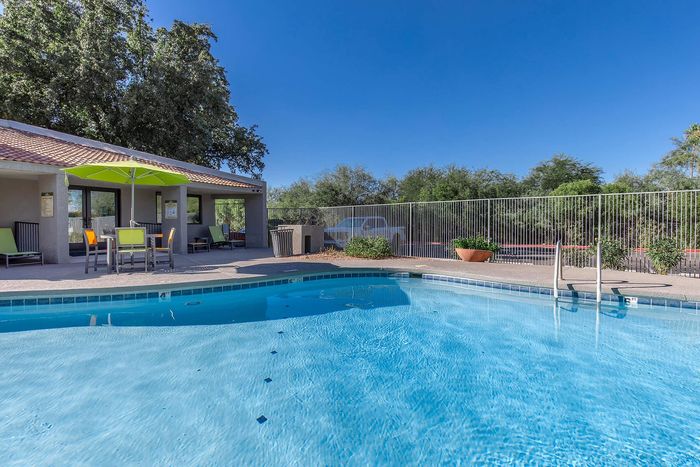 Inviting outdoor pool area with vibrant umbrella and seating, framed by lush greenery and a clear blue sky.