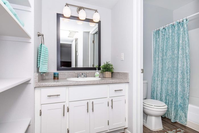 Modern bathroom featuring elegant white cabinetry, a large mirror, and a stylish patterned shower curtain.