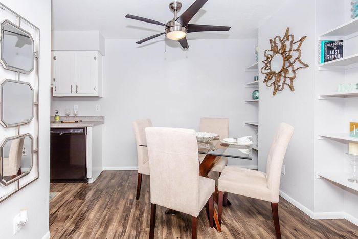 Elegant dining area with a modern glass table, plush chairs, and chic decor. Bright and inviting with a stylish ceiling fan and wood flooring.