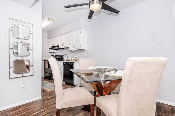 Modern dining area with elegant glass table, plush beige chairs, and sleek kitchen with white cabinetry and contemporary decor.