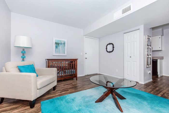 Stylish modern living room with elegant white armchair, vibrant teal accents, and sleek glass coffee table on wooden flooring.