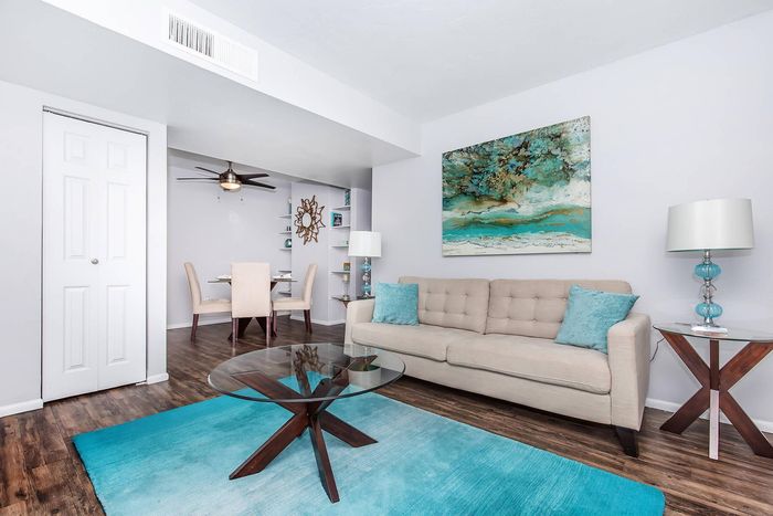 Modern living room with elegant beige sofa, vibrant turquoise accents, and sleek glass coffee table, seamlessly flowing into a chic dining area with stylish decor.