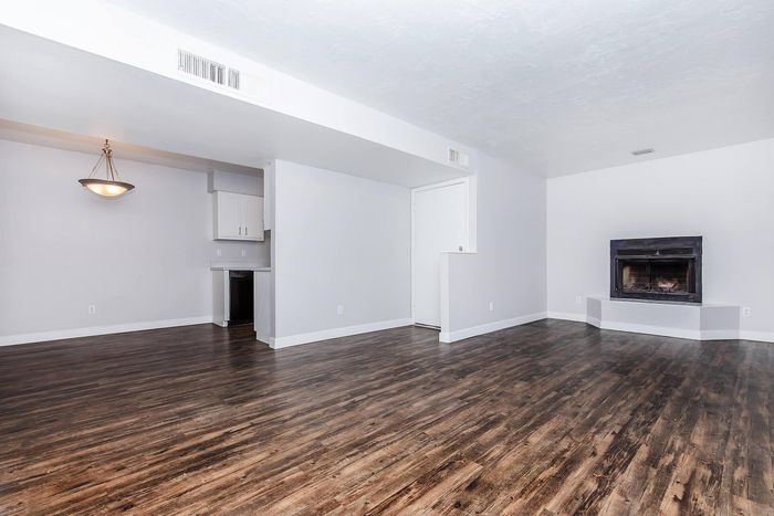 Spacious living area with elegant hardwood floors, sleek white walls, and a cozy corner fireplace, perfect for relaxation.