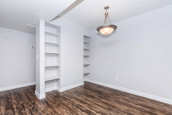 Bright and airy room with modern pendant lighting and elegant built-in shelving, complementing rich wood flooring.