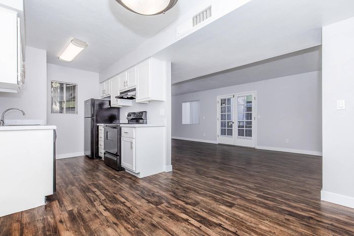 Sleek apartment interior showcasing a modern kitchen with white cabinetry and a seamless open-concept living space with elegant wood flooring.
