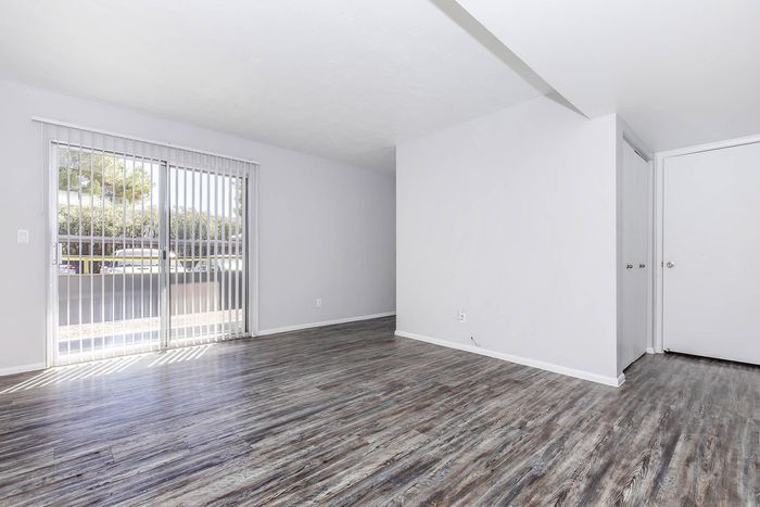 Bright, modern living space featuring sleek flooring and expansive windows with vertical blinds overlooking a lush outdoor scene.