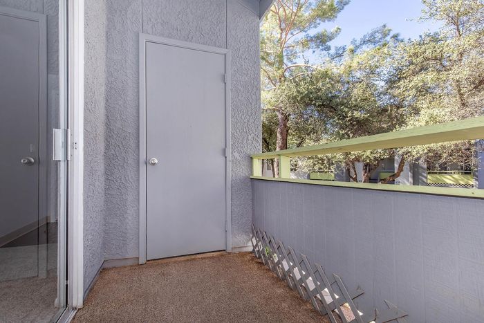 Charming outdoor balcony with textured walls, offering a peaceful view of lush trees, perfect for relaxation.