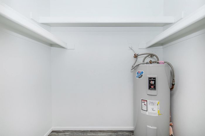 Spacious utility closet with sleek white shelves and a modern water heater, perfect for efficient storage solutions.