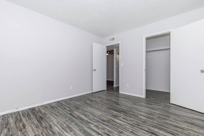 Modern bedroom with sleek wood flooring, neutral walls, ample closet space, and a bright ambiance.