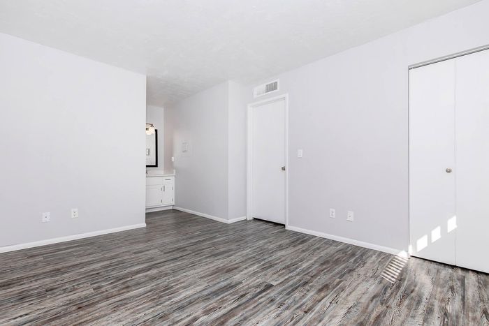 Bright and spacious empty room with elegant wood-style flooring and modern white walls, featuring an open vanity area and ample natural light.