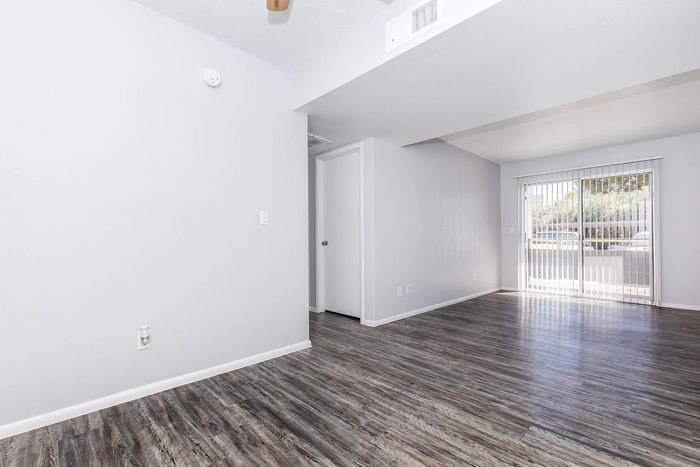 Bright and spacious living area with modern laminate flooring and large sliding glass doors opening to a scenic outdoor view.