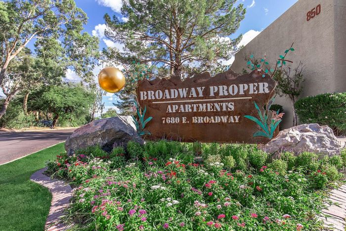 Inviting entrance sign for Broadway Proper Apartments, surrounded by vibrant landscaping and lush greenery on a sunny day.