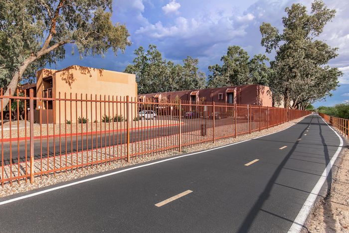 Charming apartment complex with terracotta facade, surrounded by lush trees, and featuring a bike-friendly pathway for modern living.