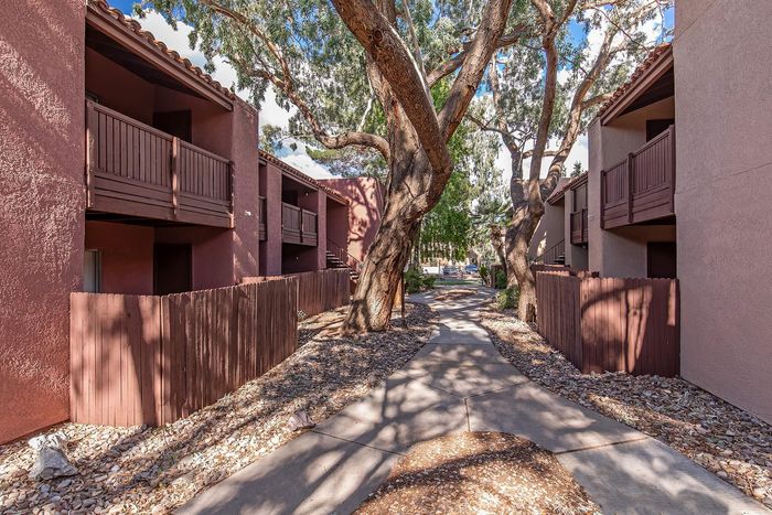Charming walkway between two-story apartment buildings, shaded by mature trees and featuring private balconies.