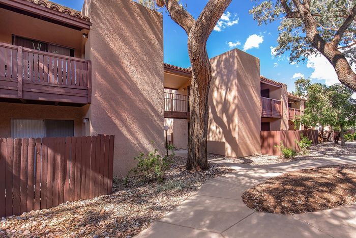 Charming apartment exterior with warm earth tones, private balconies, and shaded walkways beneath lush trees.