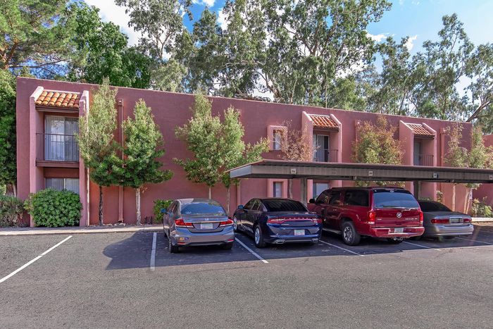 Charming apartment exterior with lush greenery and covered parking, showcasing modern architecture in a serene setting.