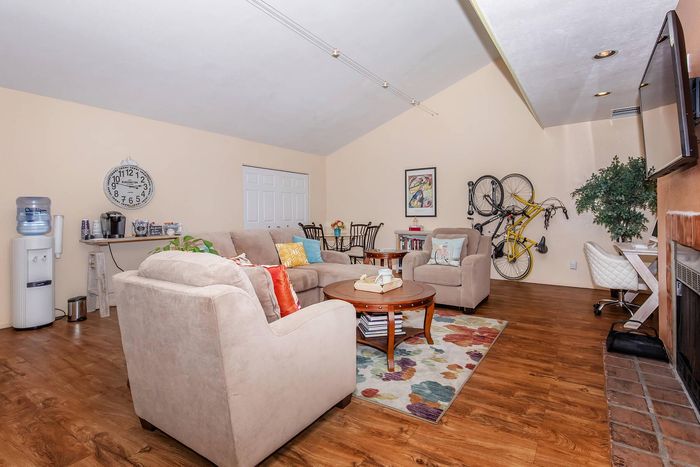 Inviting living room with cozy beige sofas, vibrant cushions, and a stylish coffee table on a floral rug; modern decor includes a wall-mounted bicycle, chic wall art, and a large clock adding charm.