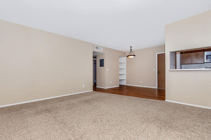 Welcoming living area with plush carpet, elegant chandelier, and convenient kitchen pass-through in a modern apartment.