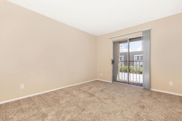 Bright, minimalistic room with neutral walls, plush carpet, and a large sliding glass door opening to a charming balcony.