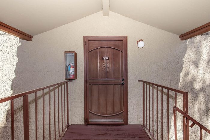 Inviting entrance to Apartment 106 with a charming wooden door, nestled in a cozy walkway enhanced by warm stucco textures and modern lighting.