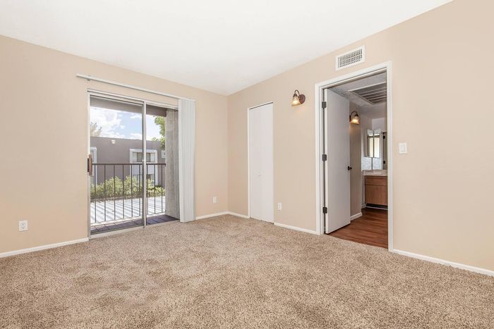 Bright and airy bedroom with plush carpeting, large sliding glass doors opening to a balcony, and easy access to an adjacent bathroom.