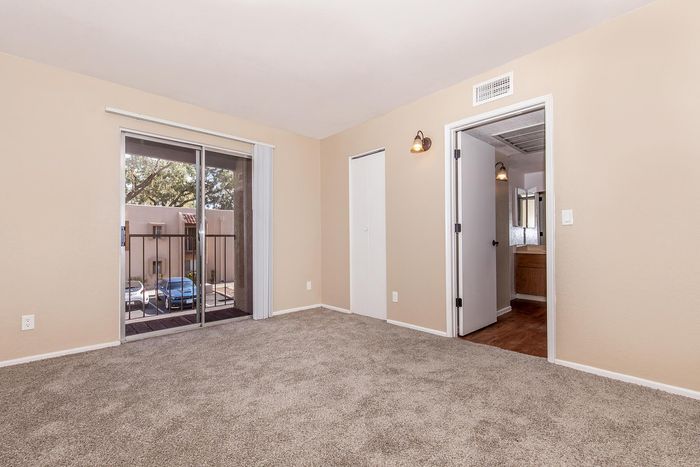 Bright bedroom with plush carpet and balcony access, offering a spacious closet and convenient ensuite entrance.