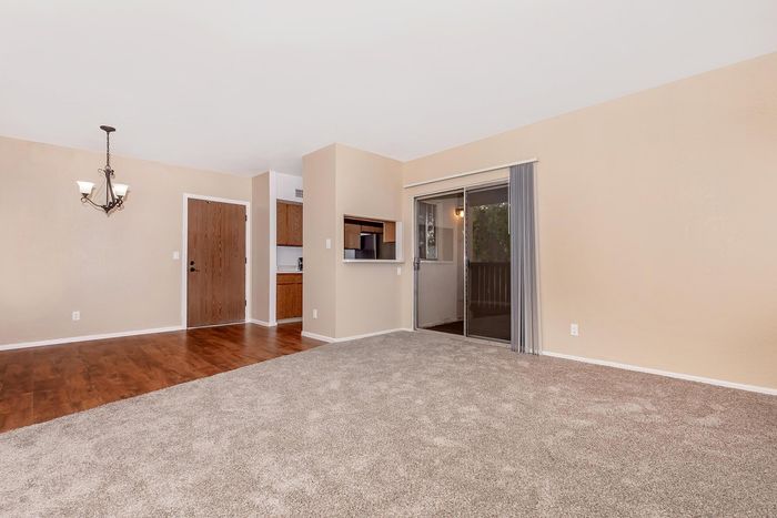 Inviting living space with plush carpeting, hardwood flooring, and elegant lighting, adjacent to a cozy kitchen and sliding doors leading to a serene balcony.