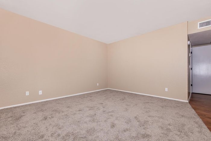 Inviting, carpeted corner room with modern beige walls, featuring an adjacent space with an elegant wooden floor.