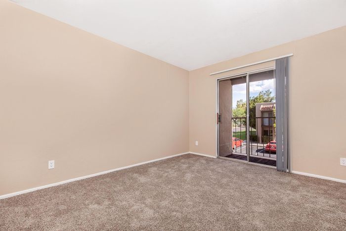 Inviting and tranquil apartment bedroom with plush carpet, neutral walls, and a sliding glass door leading to a cozy balcony.