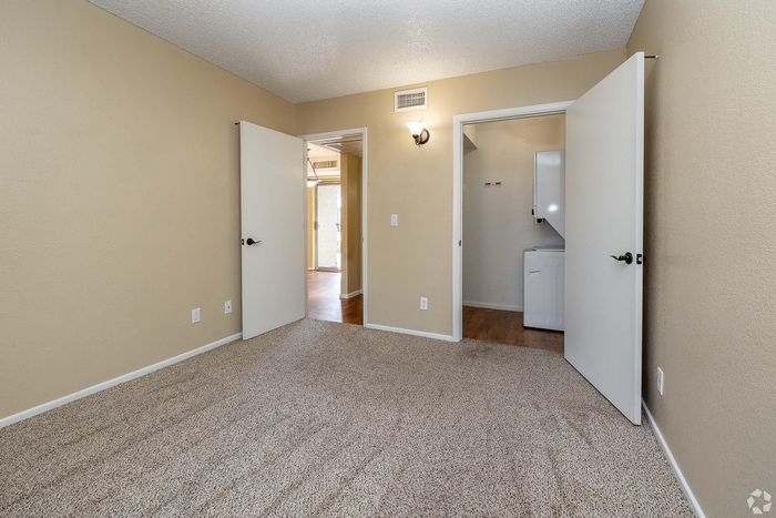 Bright, spacious bedroom with plush carpet, dual-door entry, and access to a practical laundry area.