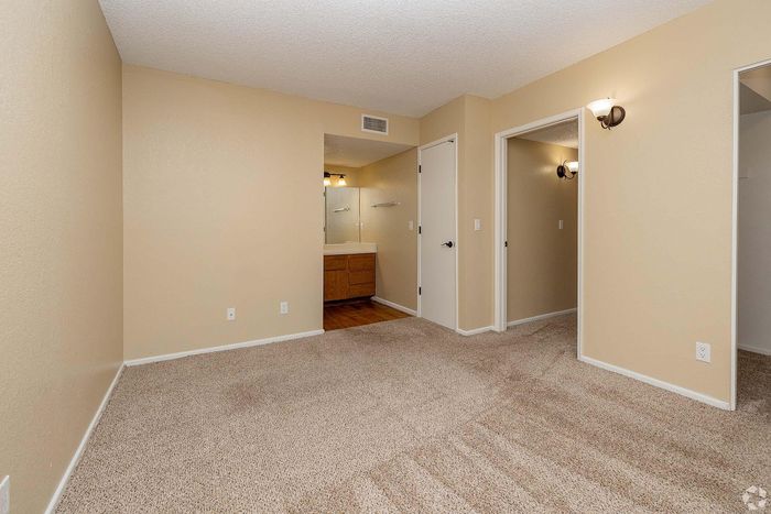 Inviting bedroom showcasing soft beige walls, plush carpeting, and a glimpse of a modern en-suite bathroom with elegant lighting.