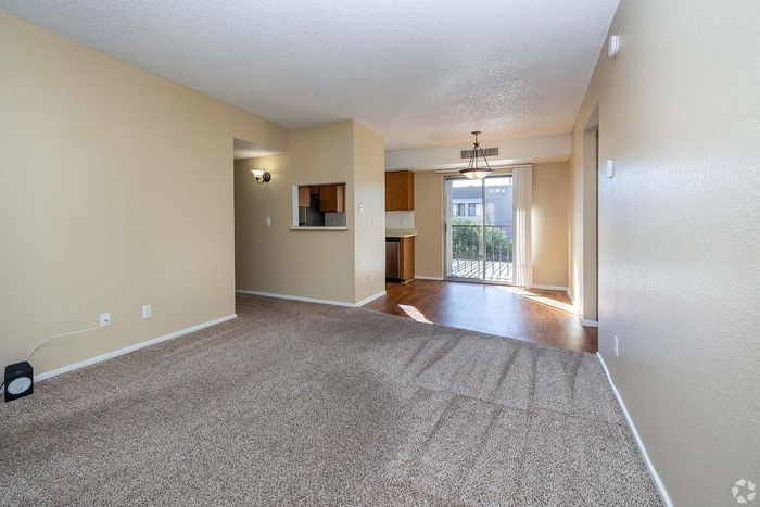 Inviting apartment interior featuring a bright living area with plush carpet, a cozy kitchen nook, and sunlit patio doors leading to a scenic balcony view.
