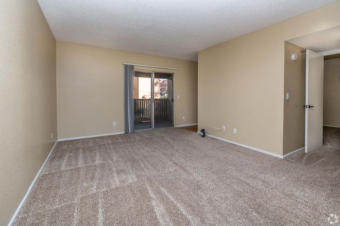Spacious living room with plush carpeting and sliding glass doors leading to a private balcony.