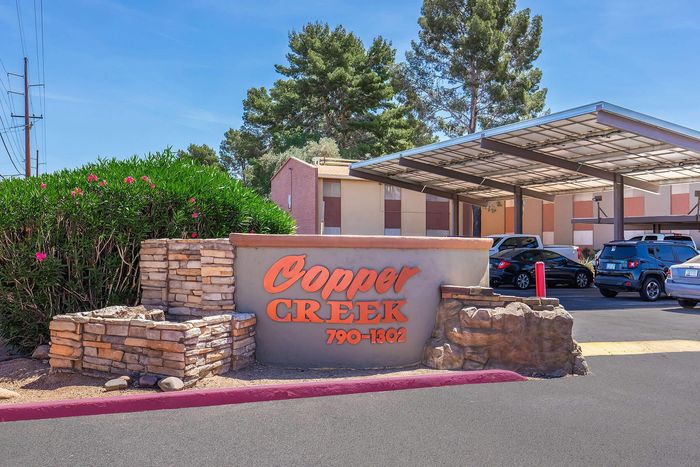 Inviting entrance to Copper Creek, featuring a beautifully landscaped stone sign and modern covered parking area.