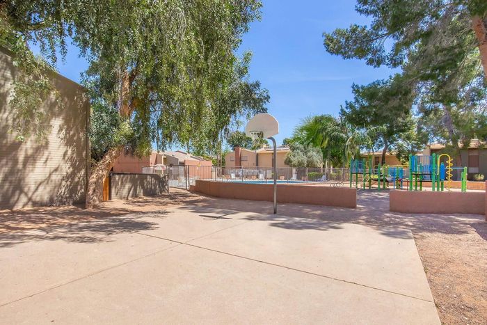 Bright community area with a basketball court and vibrant playground surrounded by lush greenery.