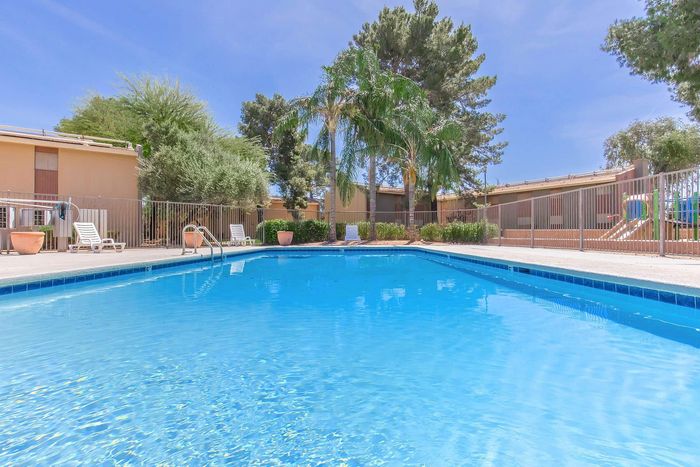 Inviting outdoor swimming pool with crystal-clear water, surrounded by lush greenery and sun loungers, offering a perfect relaxation spot under the blue sky.