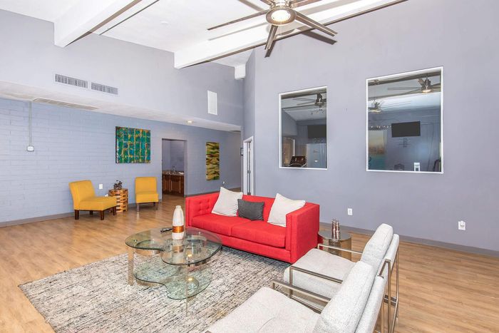 Modern living room with a vibrant red sofa, stylish glass coffee table, and sleek yellow chairs, featuring contemporary decor and spacious design.