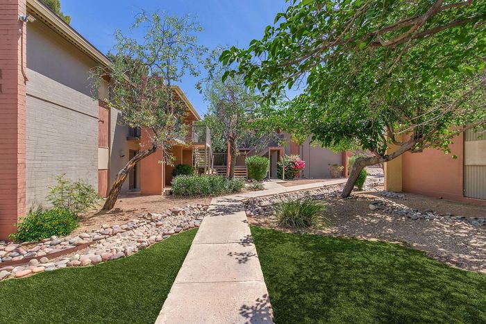 Charming apartment complex exterior with lush greenery, vibrant flowers, and inviting walking paths.
