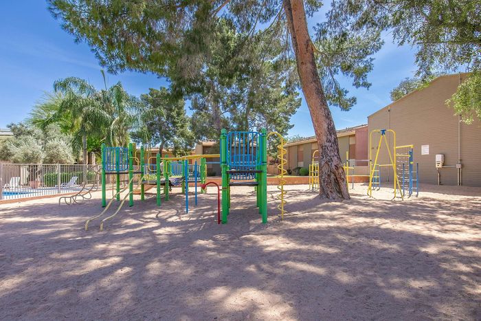 Inviting apartment community playground with colorful slides and climbing structures under the shade of tall trees.