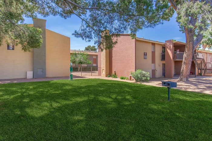 Charming apartment complex with lush green lawns, mature trees, and a warm, inviting exterior under a clear blue sky.