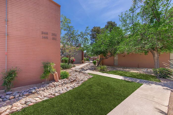 Charming courtyard view with lush greenery and vibrant landscape, featuring a brick building facade and serene walkway.