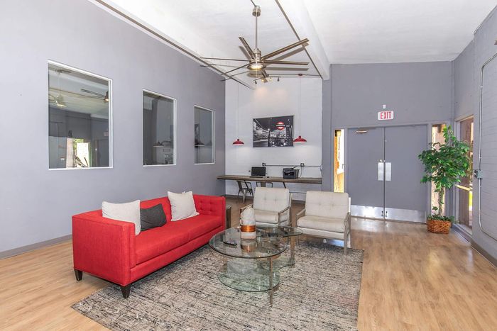 Modern lounge area with vibrant red sofa, stylish glass coffee table, and elegant workspace, offering a blend of comfort and sophistication.