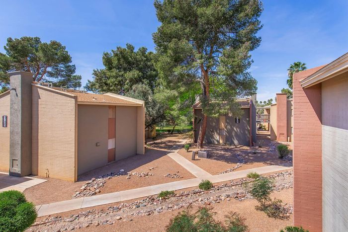 Charming desert-style apartment complex with spacious walkways, lush green trees, and inviting architectural design.