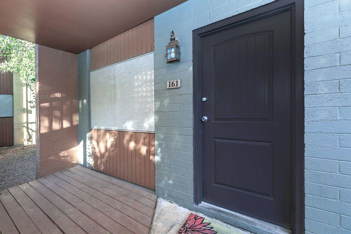 Charming apartment entrance with a sleek black door, chic lantern lighting, and a welcoming wooden deck.
