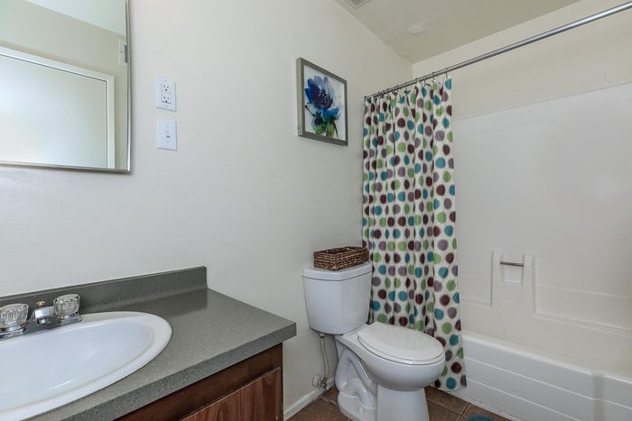 Bright and modern bathroom with sleek gray countertop, vibrant polka dot shower curtain, and elegant wall art.