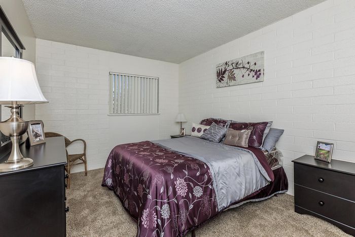 Inviting bedroom with elegant purple bedding, cozy lamp-lit dresser, and serene wall art, perfect for relaxation.